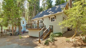 A rustic cabin with a wooden staircase leading to a deck, surrounded by trees.
