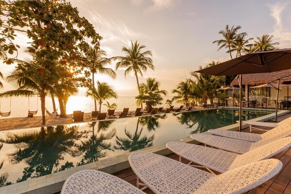A poolside area with lounge chairs, a swing, and palm trees.