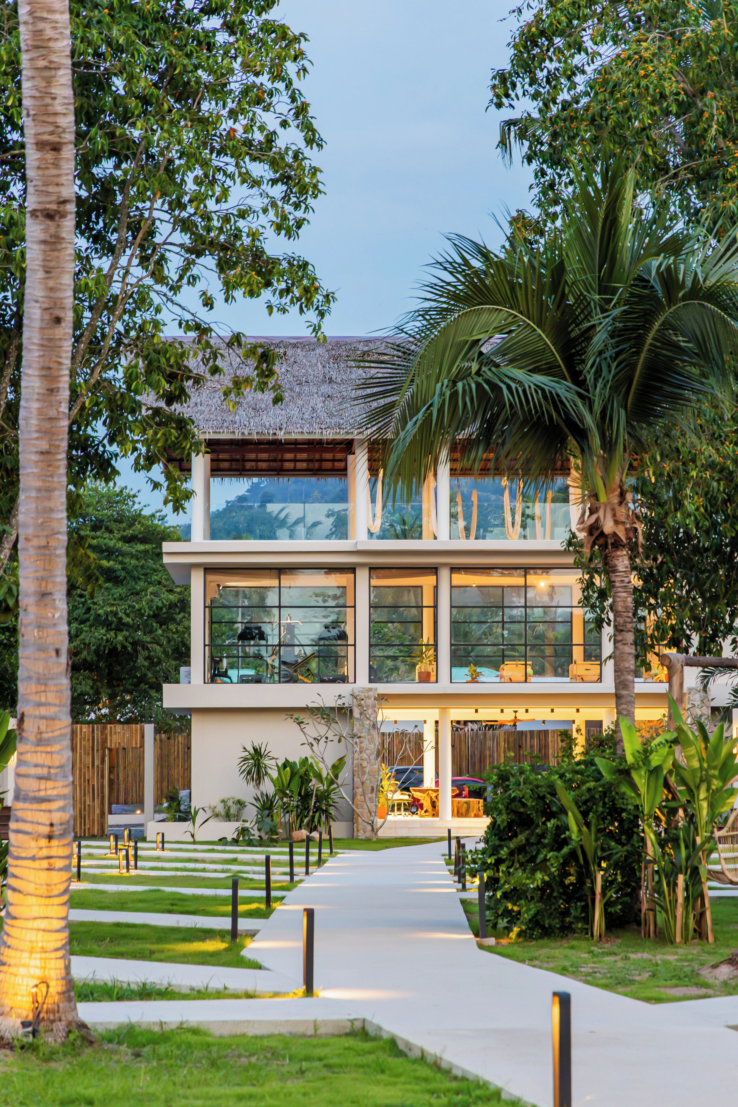 A modern two-story building with large windows, a pathway leading to the entrance, and surrounding greenery.
