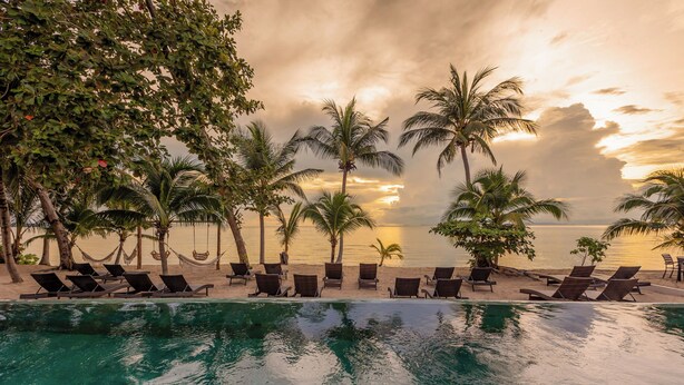 A poolside area with lounge chairs and palm trees, overlooking a beach and ocean. - Samaraya Wellness Resort (Koh Samui)