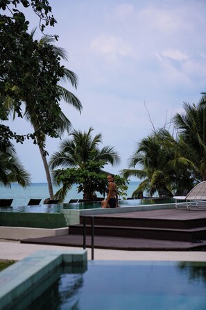 A pool area with palm trees, a view of the ocean, and a person walking.
