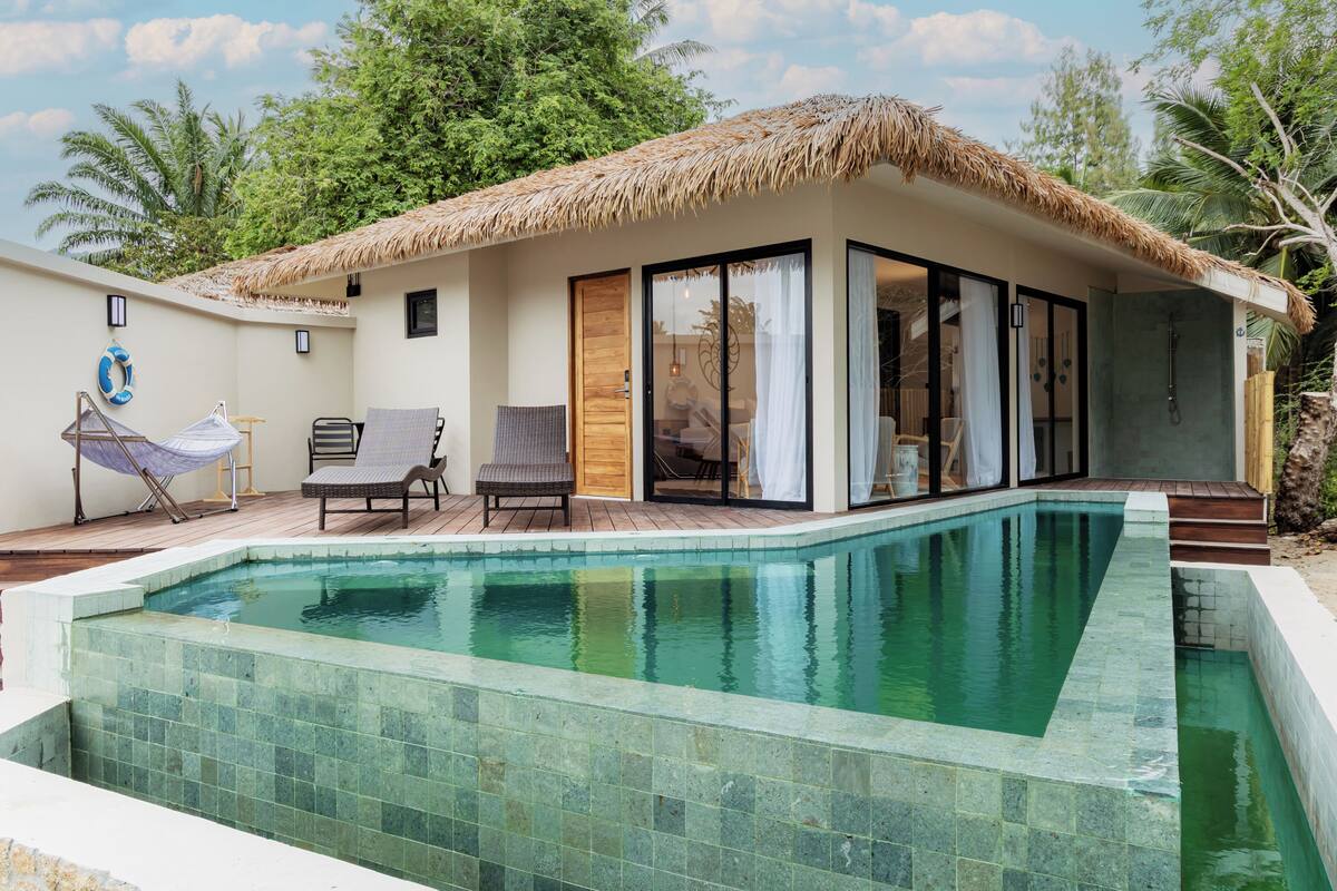 A poolside area with a thatched roof, a lounge chair, a sunbed, and a view of the pool.