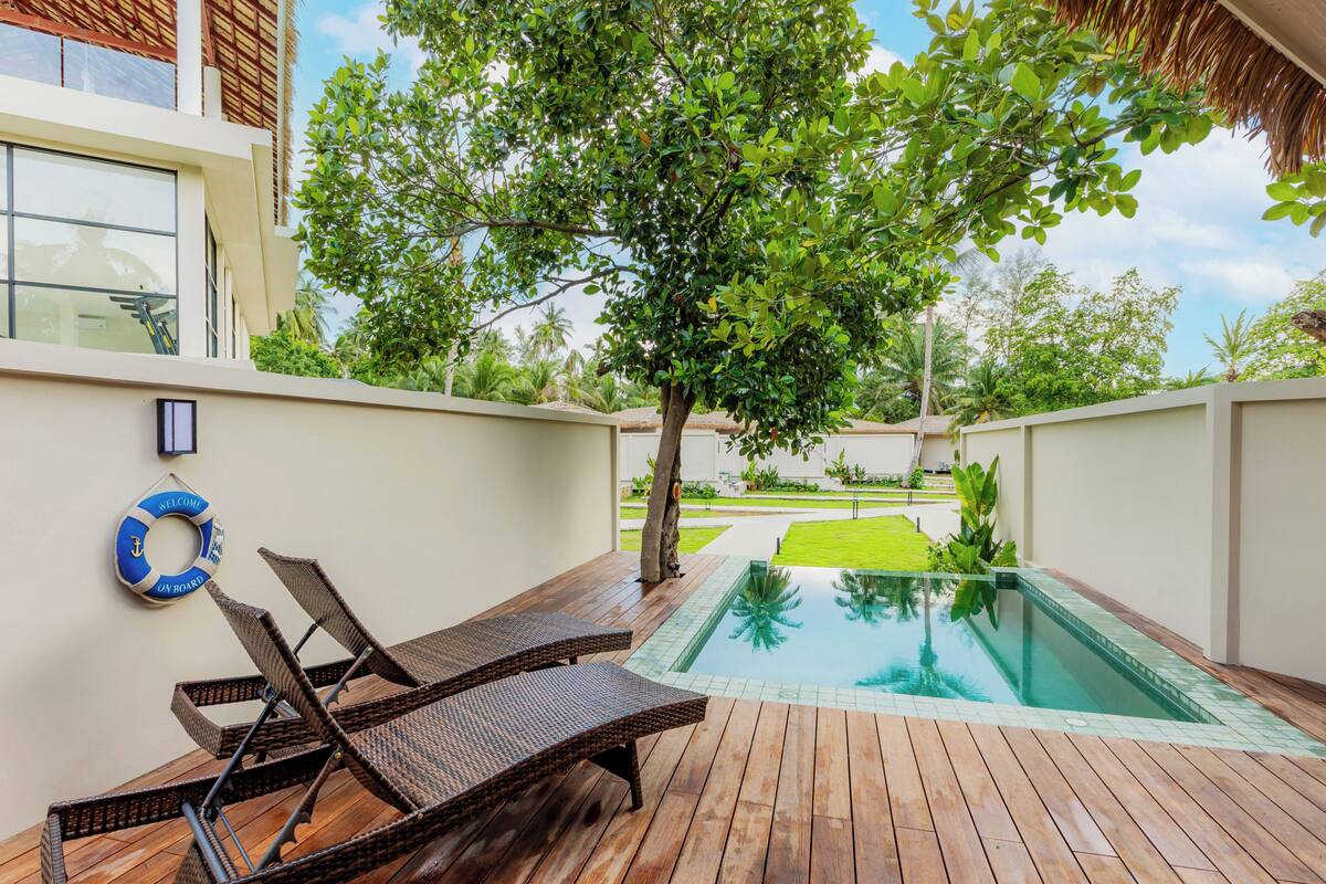 A pool area with lounge chairs, a lifebuoy, and a tree.