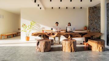 Un interior moderno con una mesa de madera central, dos taburetes, una planta en maceta y una pared de piedra.