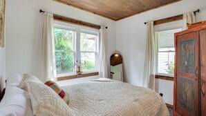 A bedroom with a large bed, two windows with curtains, a wooden ceiling, and a wooden cabinet with artwork. - < 1 Mi to Downtown Arcadia: Tranquil Wooded Escape (Arcadia)