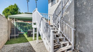 Um imóvel residencial com área externa coberta, escada e vista para uma palmeira e vegetação.