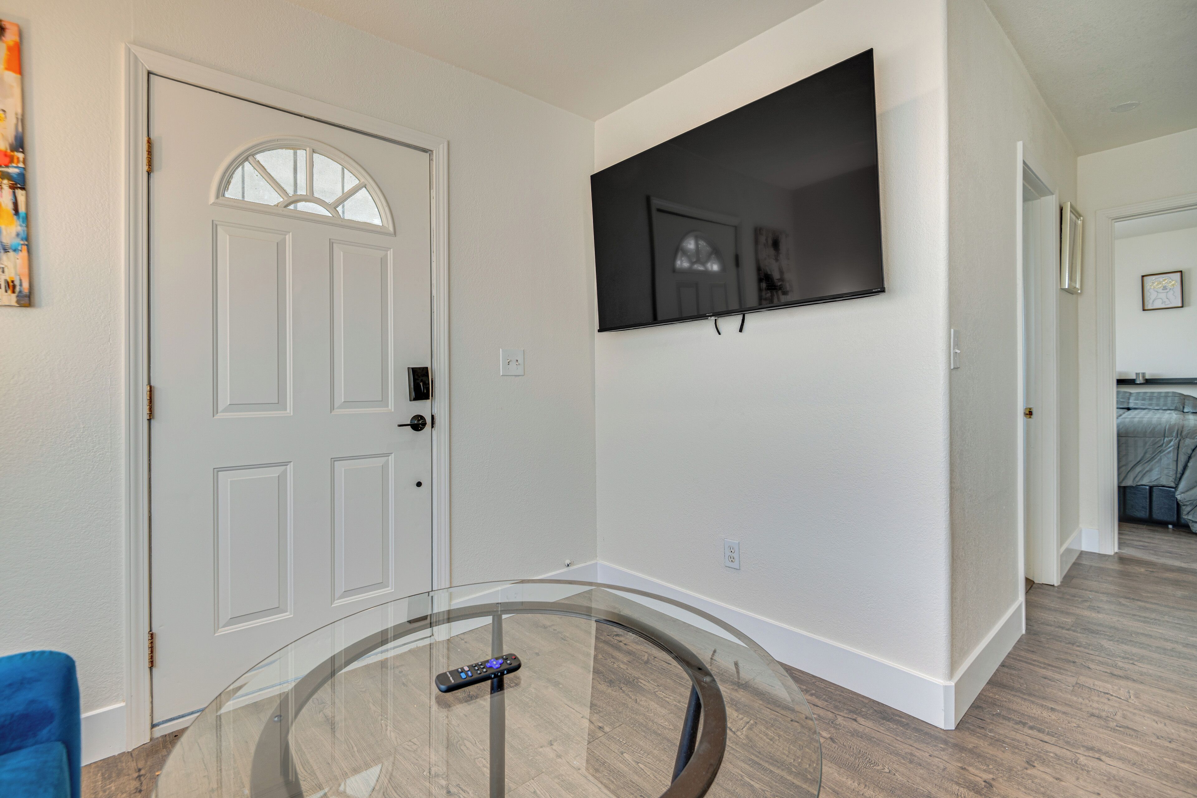 A modern living room with a glass coffee table, a mounted flat-screen TV, and a white door with a glass panel.
