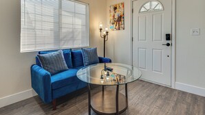 Sala de estar com um sofá azul, uma mesa de centro de vidro, uma porta e um quadro na parede.