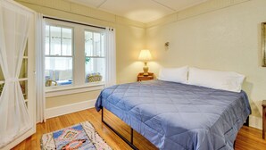 Un dormitorio con cama, ventana con cortinas, lámpara y suelo de madera.