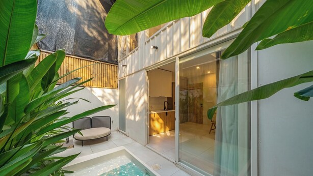 A modern outdoor pool area with a glass door leading to a room, surrounded by lush greenery.