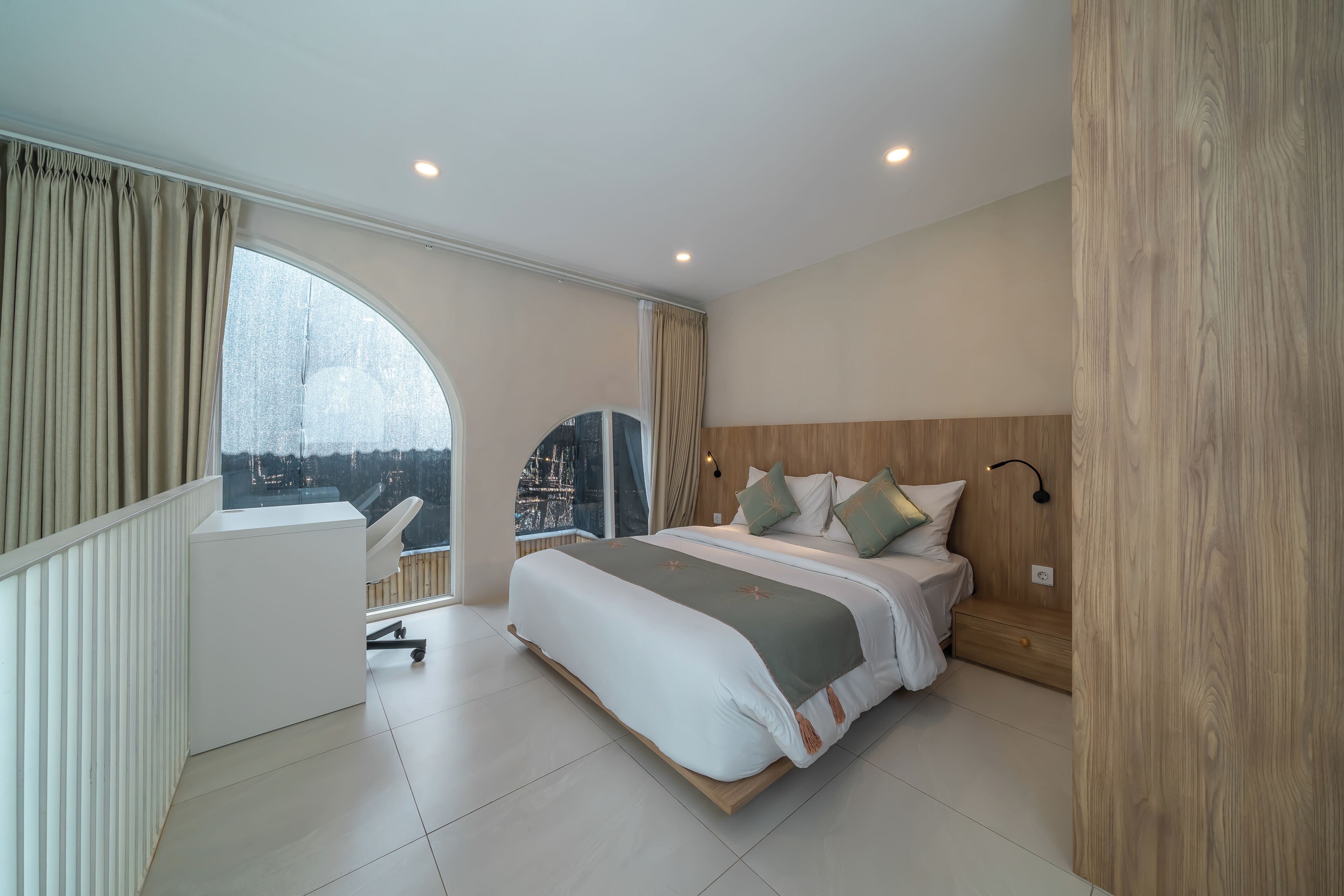 A modern bedroom with a large bed, a desk, and a view of a cityscape.