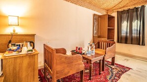 Ein Zimmer mit einem Holzesstisch, Stühlen, einer Kaffeemaschine und einer Ablage mit Snacks. Es gibt ein Fenster mit Vorhängen und eine verzierte Decke.