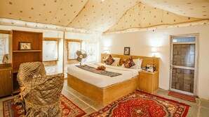Ein geräumiges Schlafzimmer mit einem großen Bett, einem Holznachttisch, einem Ventilator und einem roten Teppich mit Muster.
