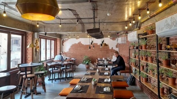 A restaurant with tables, chairs, hanging lights, brick walls, and potted plants. - The Nanee (Bhaktapur)