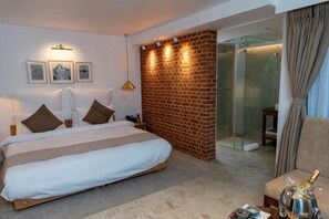 A hotel room with a bed, a glass partition, a seating area, and a brick wall. - The Nanee (Bhaktapur)