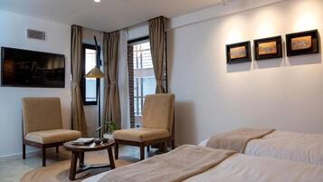 A hotel room with two beds, a desk, two chairs, a TV, and artwork on the wall.