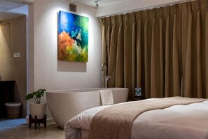A modern bathroom with a freestanding bathtub, a potted plant, and a large painting on the wall. - The Nanee (Bhaktapur)