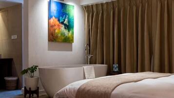 A modern bathroom with a freestanding bathtub, a potted plant, and a painting on the wall.