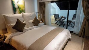 A large bed with white linens and a beige accent, a painting on the wall, and a balcony with a table and chairs. - The Nanee (Bhaktapur)
