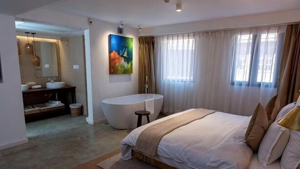 A modern bedroom with a large bed, a bathtub, and a separate bathroom with a vanity. - The Nanee (Bhaktapur)