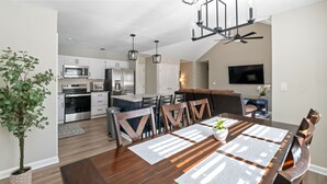A modern kitchen with stainless steel appliances, a dining area with a wooden table and chairs, and a ceiling fan.