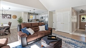 A modern living room with a brown sectional sofa, a dining table with chairs, and a kitchen in the background.