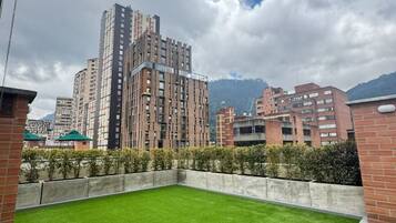 Un toit-terrasse recouvert de gazon synthétique, entouré d’immeubles de grande hauteur et surplombant un ciel nuageux.