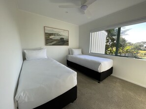 Ein Schlafzimmer mit zwei Betten, einem Deckenventilator, einem Bild und einem Fenster mit Blick.