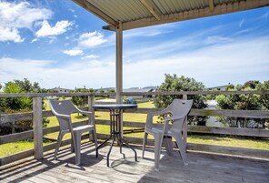 Un espacio al aire libre techado con una terraza de madera, dos sillas blancas de plástico y una pequeña mesa redonda.