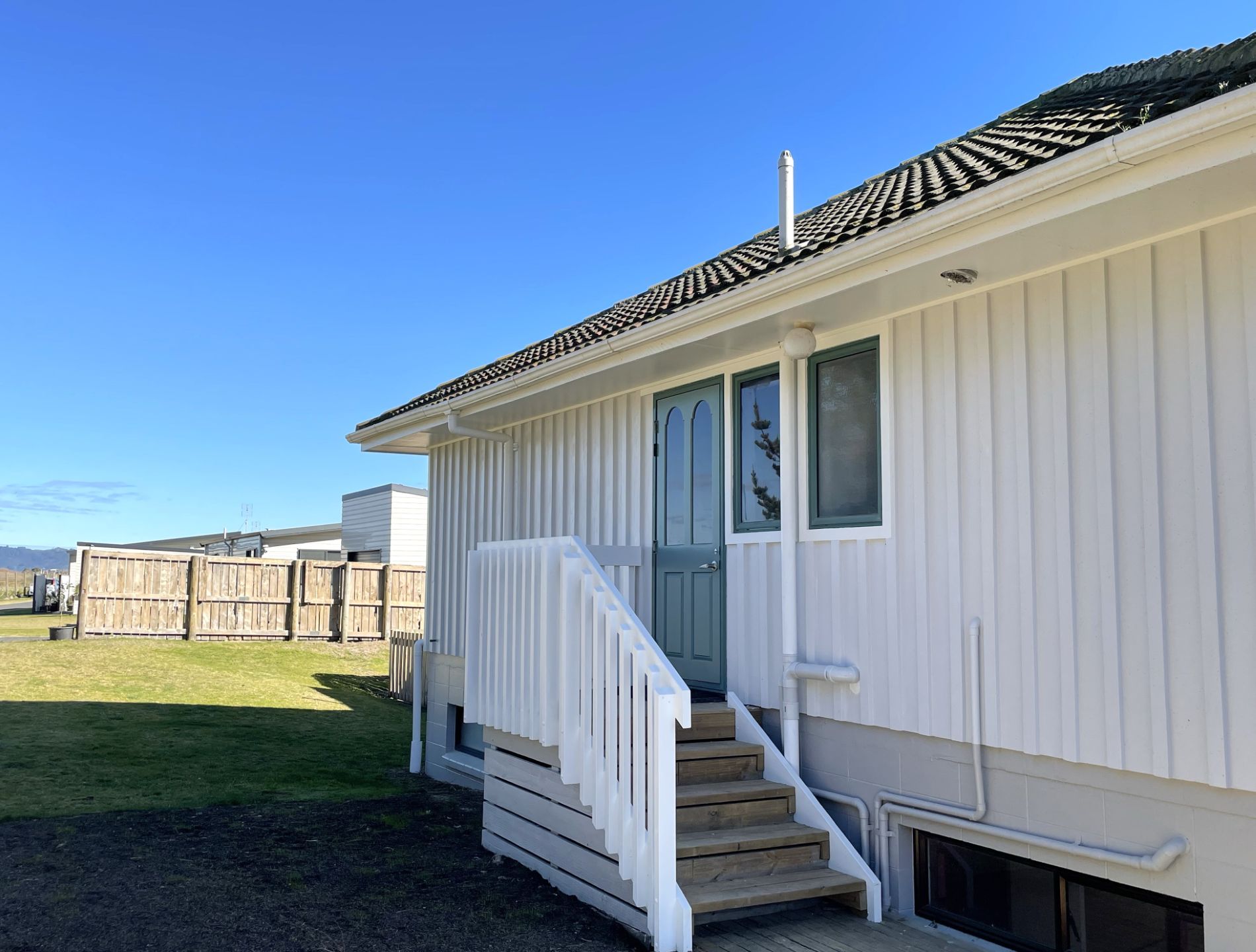 A single-story mobile home with a front porch, a set of stairs leading to the entrance, and a fenced backyard.