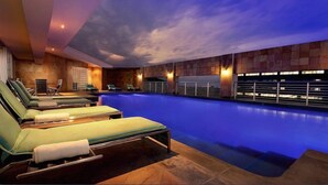 A modern indoor swimming pool with lounge chairs and a sunset sky view. - Royal Majestic Hotel (Johannesburg)