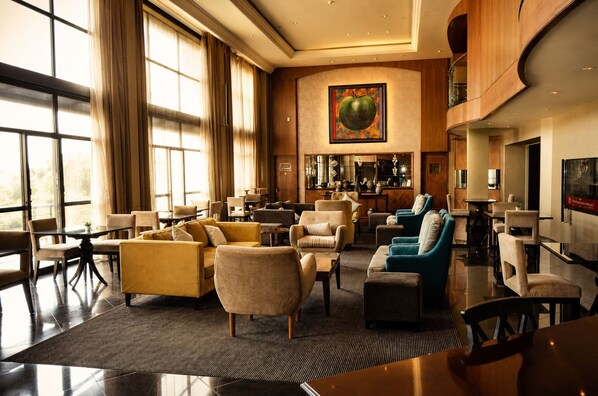 A spacious lobby with a bar area, seating arrangements, and large windows. - Royal Majestic Hotel (Johannesburg)