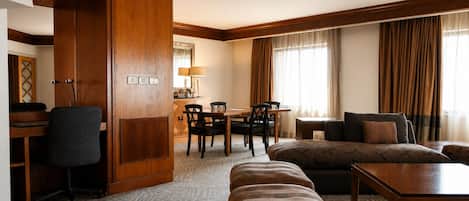 Ett hotellrum med en garderob i trä, en matplats med bord och stolar, en soffa, en pall och ett litet träbord.