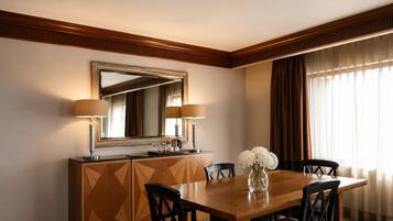 A hotel dining room with a wooden table, four chairs, a large mirror, two lamps, and a vase with flowers.
