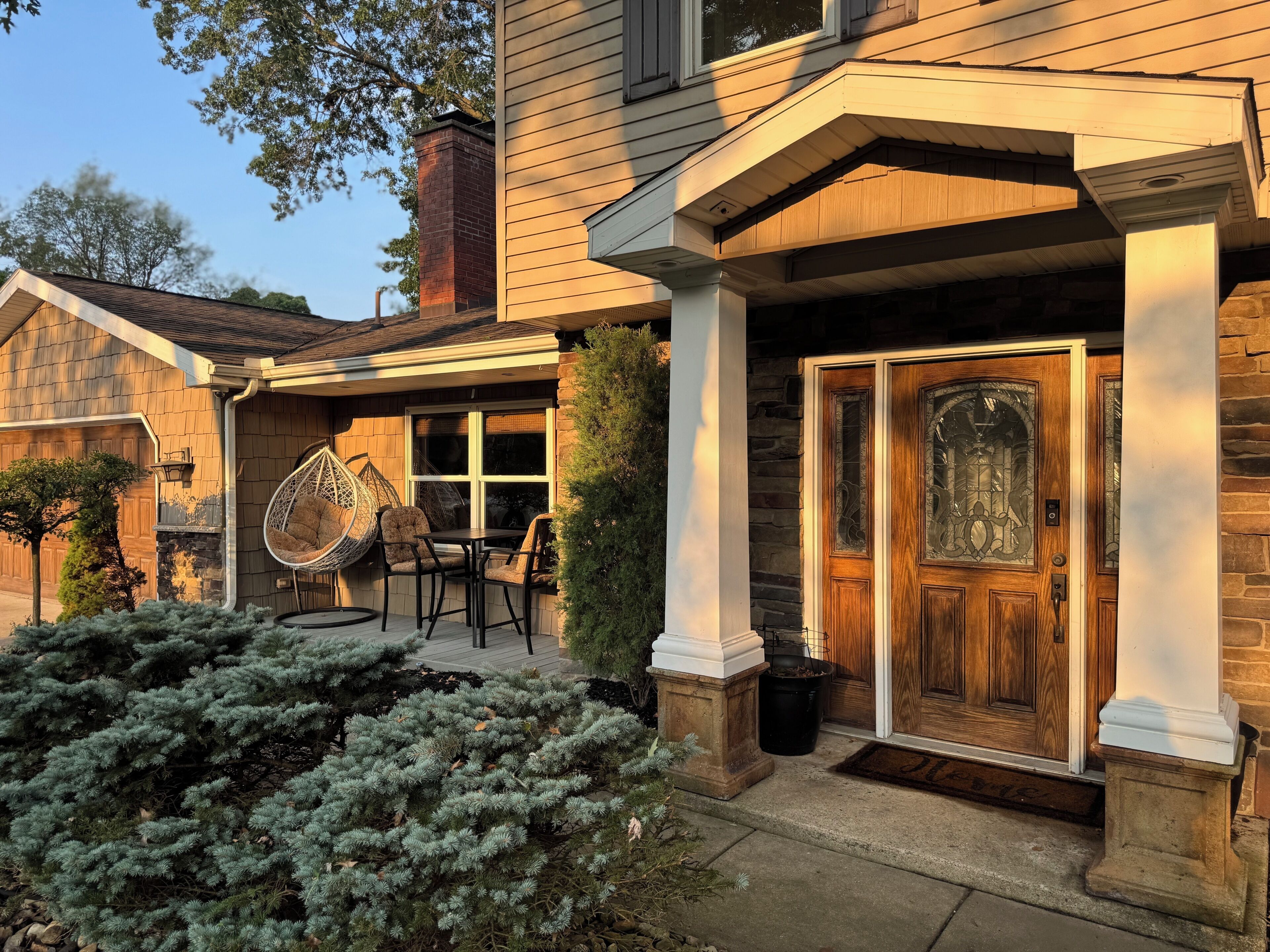 A residential house with a front porch, a wooden door with glass panels, and a hanging chair.
