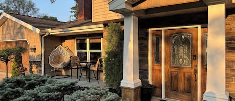 A residential house with a front porch, a wooden door with glass panels, and a hanging chair.
