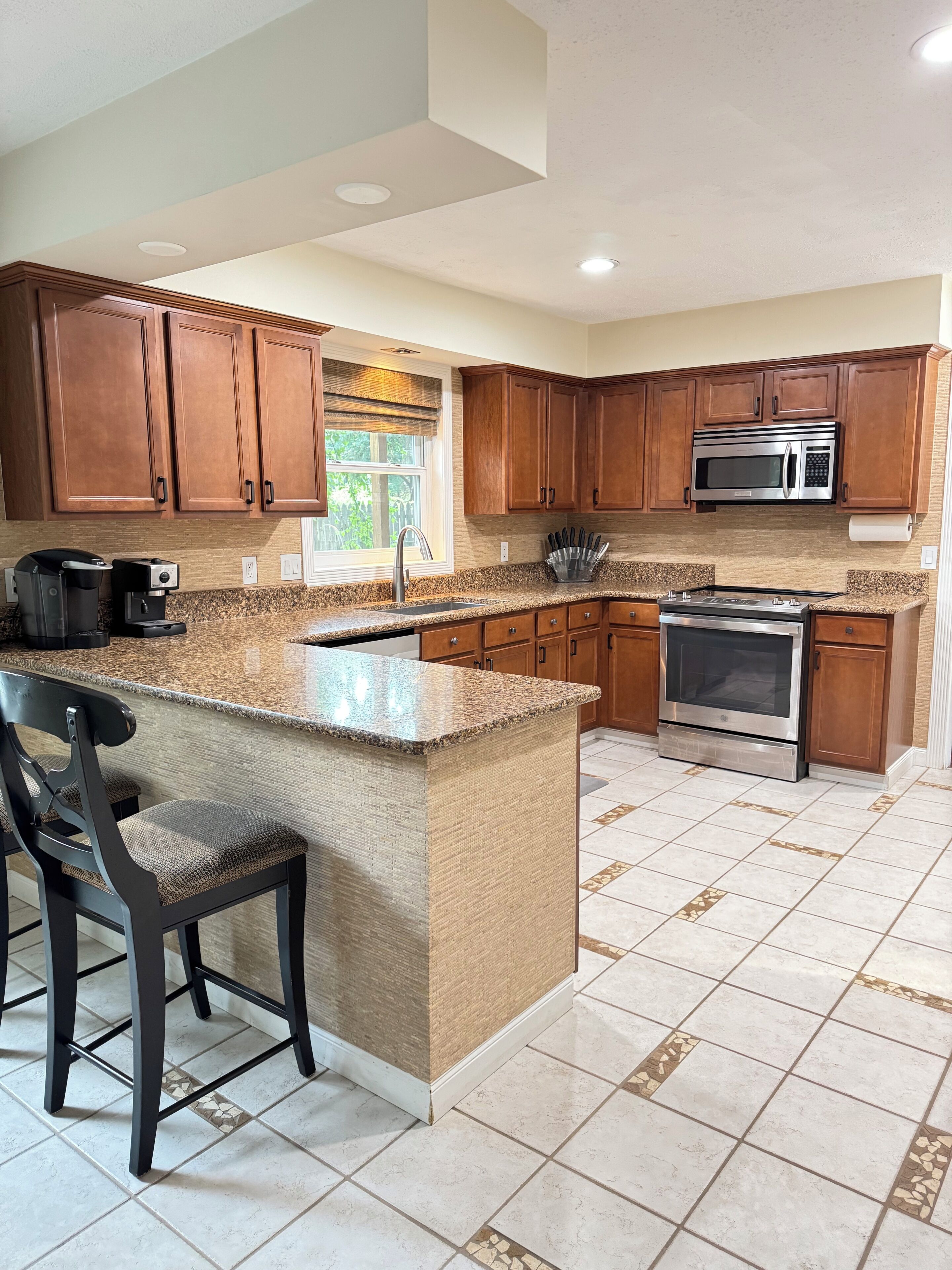 A kitchen with a central island, wooden cabinets, stainless steel appliances, and a window with a view.