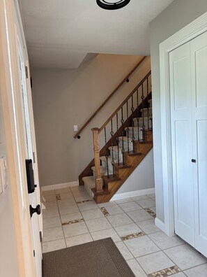 A hallway with a wooden staircase, a white door, and a patterned rug.