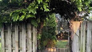 Een houten poort met een metalen hek, omgeven door een tuin met mulch en rotsen.