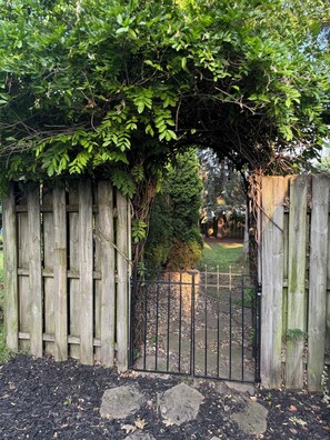 Un cancello in legno con recinzione metallica, immerso in un giardino con pacciamatura e pietre.