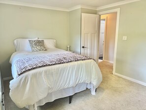 A bedroom with a bed, a nightstand, a door, and a carpeted floor.