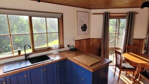 A kitchen with a wooden countertop, blue cabinets, a sink, and a dining area with a table and chairs. - Tall Trees Eco Retreat - Manna Gum Cottage (Apollo Bay)