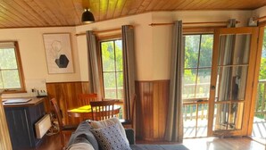 A cozy living room with a large sectional sofa, a small round table, and a dining area with a wooden table and chairs. - Tall Trees Eco Retreat - Manna Gum Cottage (Apollo Bay)