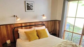 A wooden-paneled bedroom with a bed, bedside lamps, and a window with a view. - Tall Trees Eco Retreat - Manna Gum Cottage (Apollo Bay)