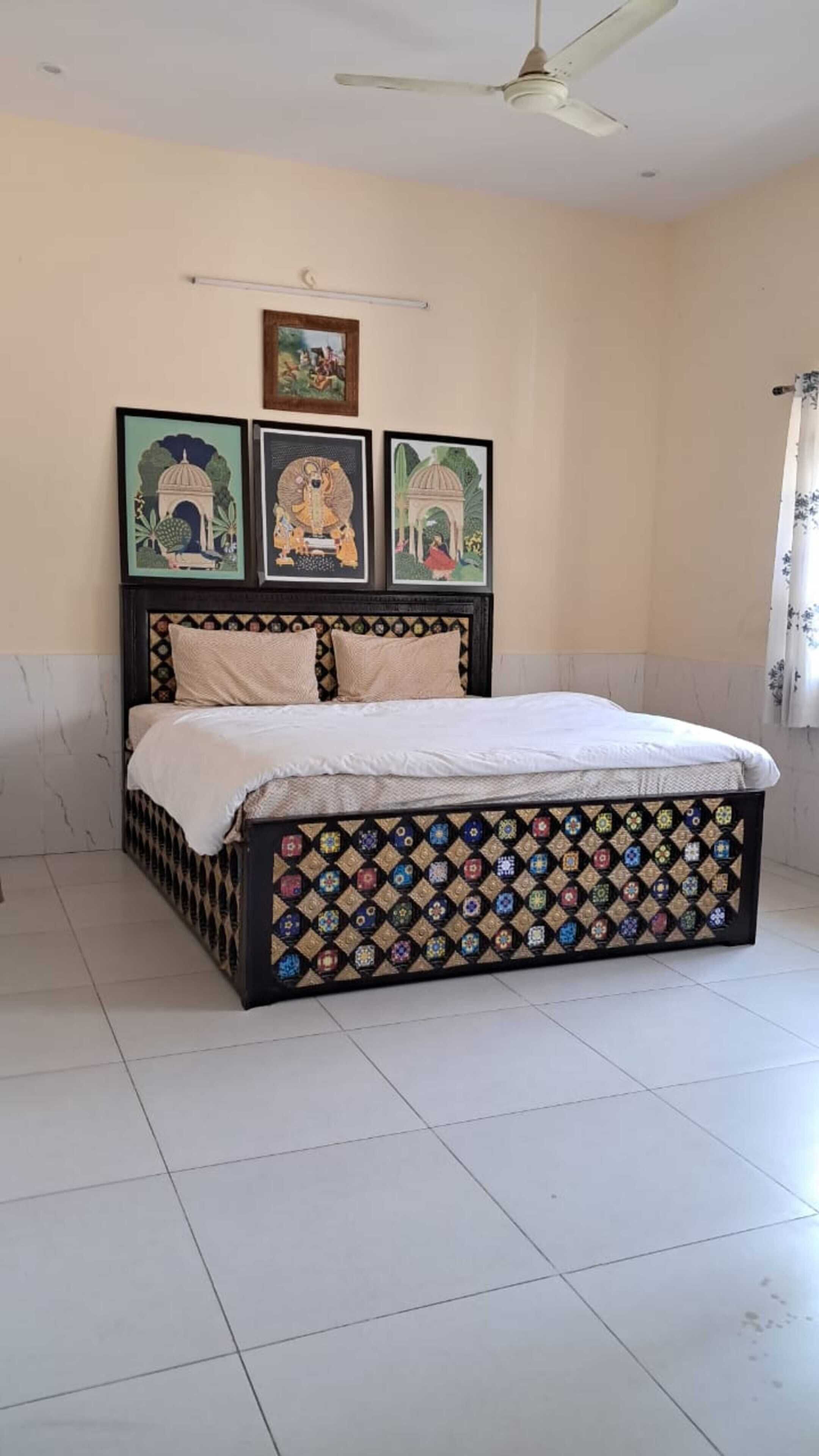 A bedroom with a bed, a ceiling fan, and three framed artworks on the wall.