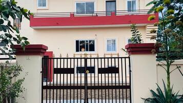 A two-story building with a red and beige facade, a gated entrance, and a sign indicating 'Virasat Holiday Home'.