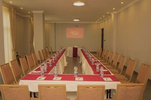 Un salón de conferencias con una larga mesa, sillas y una pantalla de proyector.