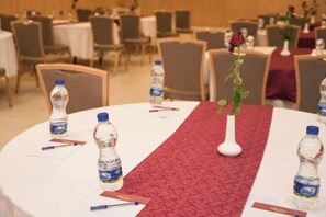 Un salón de conferencias con mesas redondas, botellas de agua, jarrones con flores y tarjetas de nombre.