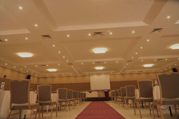 Un salón de conferencias con filas de sillas, una alfombra roja y una pantalla de proyector al frente.