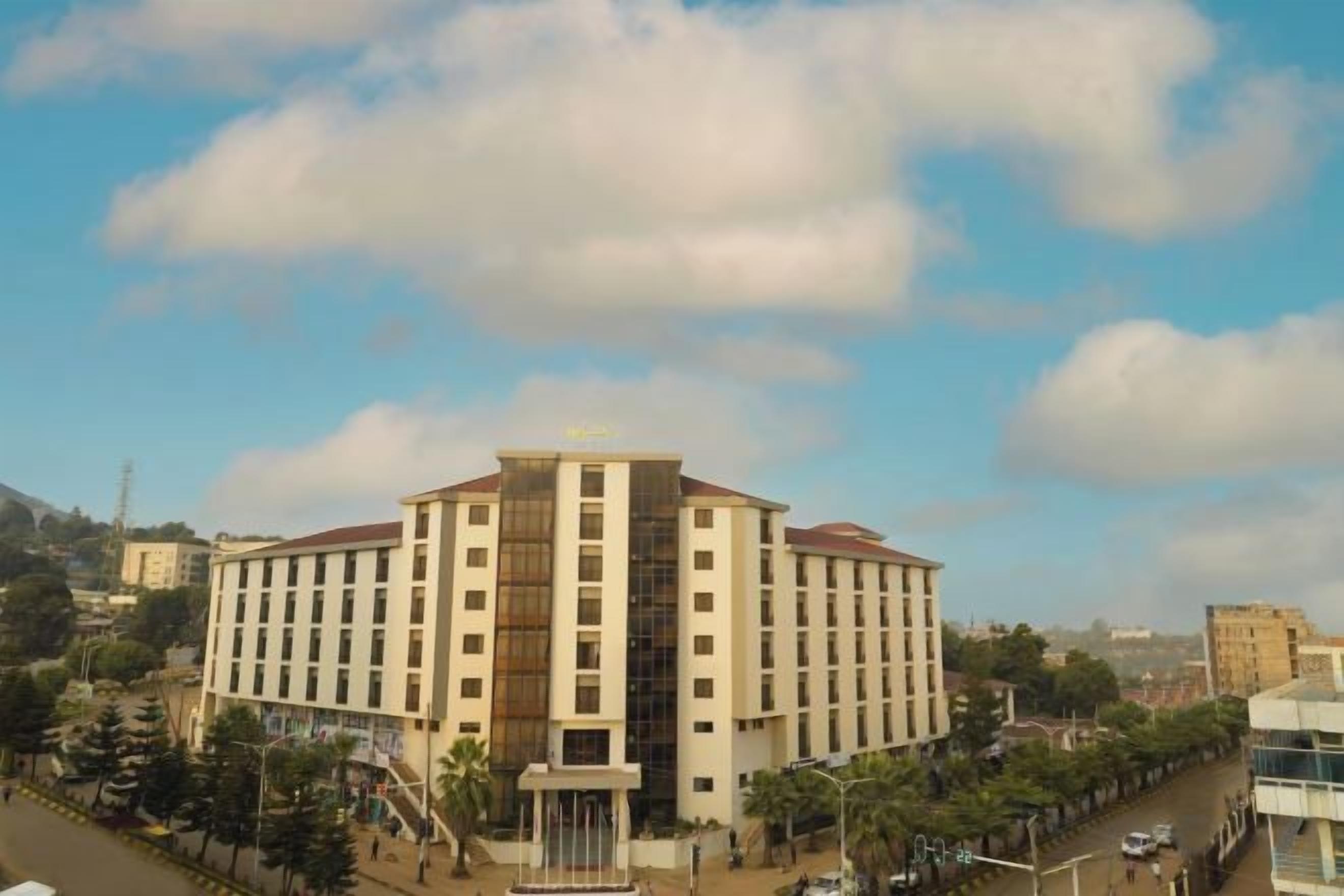 A multi-story hotel with a central atrium, surrounded by a street with parked cars and trees.